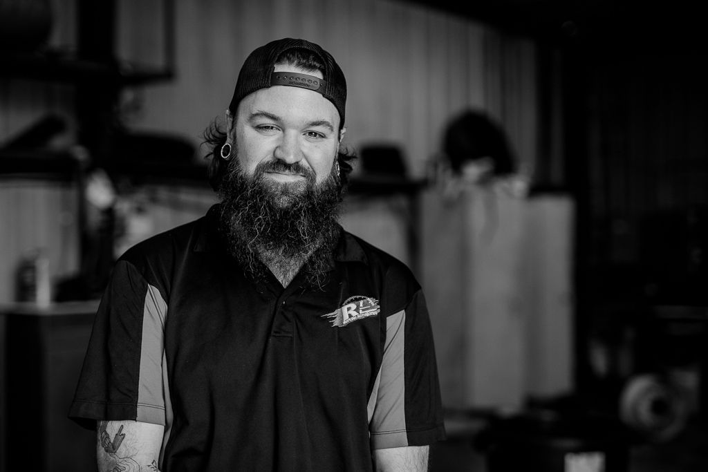 A black and white photo of a man with a beard wearing a baseball cap. | Redline Automotive