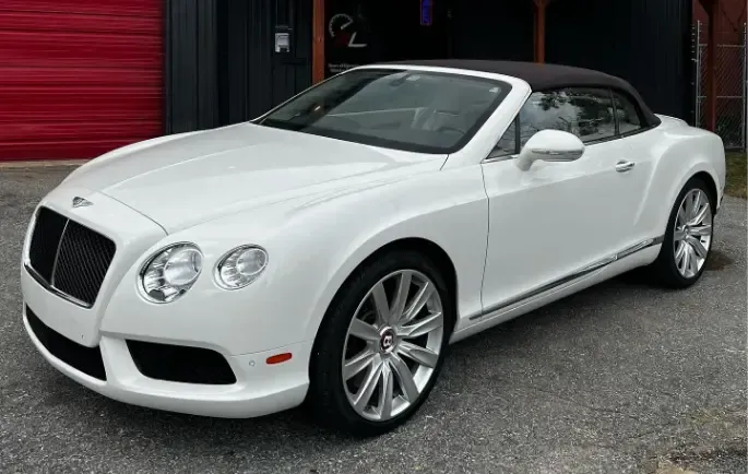 A white bentley convertible is parked in front of a red garage door | Redline Automotive