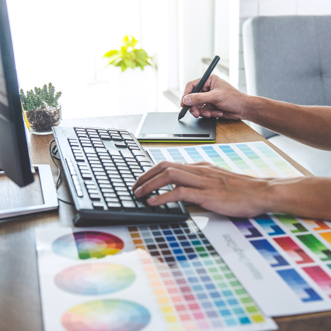 Person using a computer and a stylus on a drawing tablet, with a color palette and keyboard on the desk.