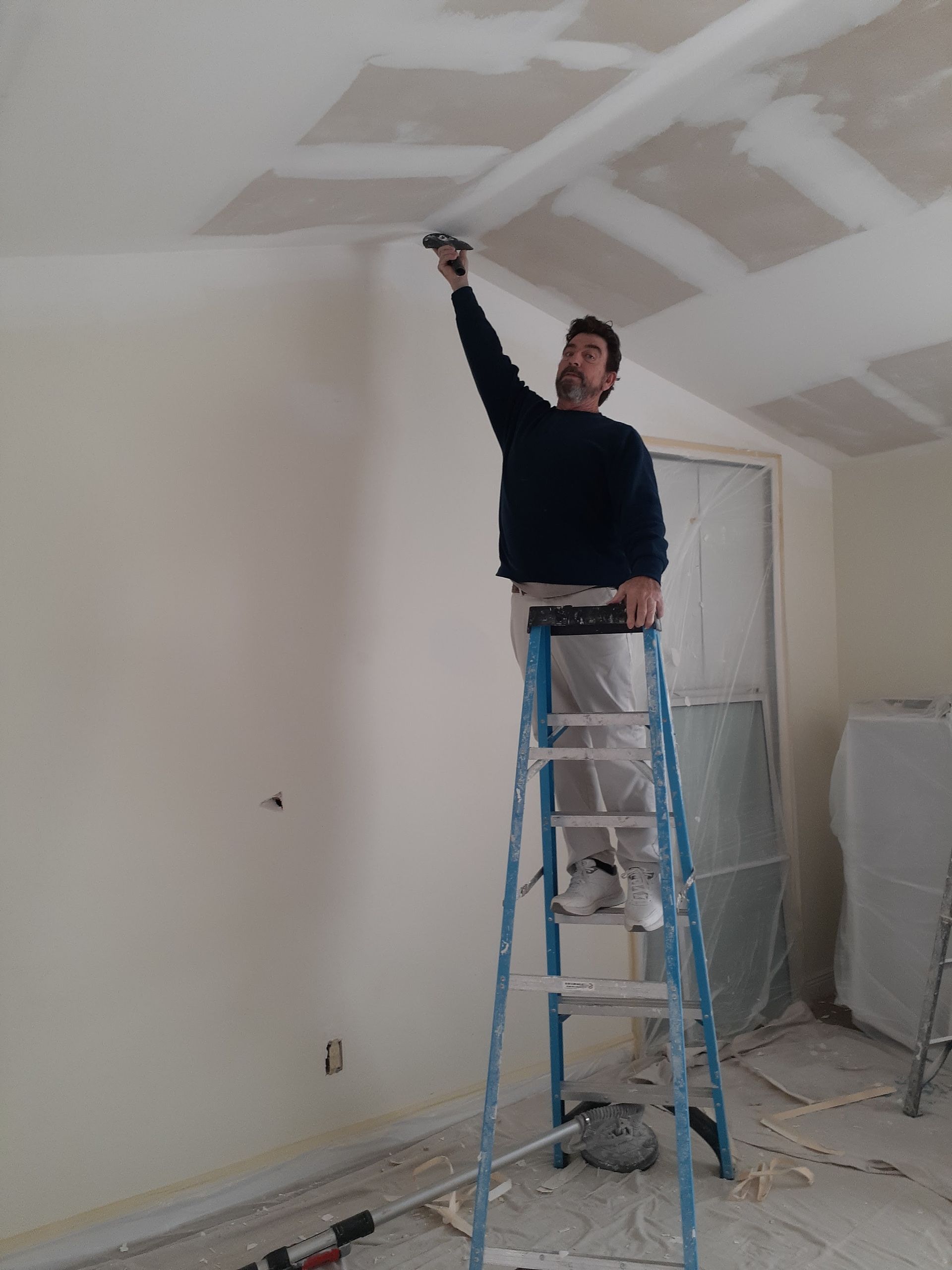 Man on ladder taping a ceiling, interior room.