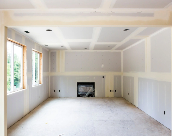 Interior of a room under construction, drywall installed; windows, fireplace, recessed lighting.