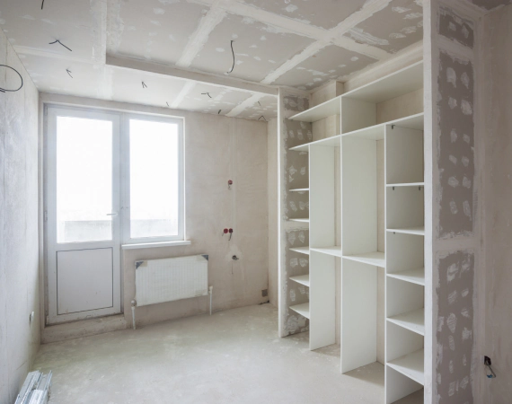 Interior of room under construction with built-in shelving, window, door, and unfinished walls.