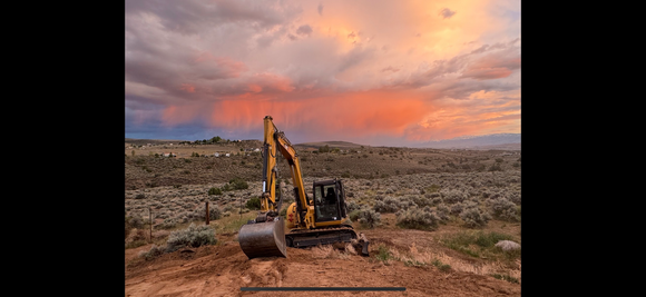 A bulldozer is digging in the dirt in the desert at sunset.