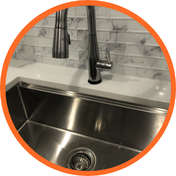Stainless steel kitchen sink with faucet and marble-patterned backsplash.