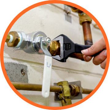 Person using a wrench to tighten a brass fitting on copper plumbing in a utility room.