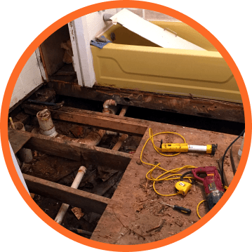 Bathroom renovation in progress: exposed subfloor, yellow tub, tools, pipes, wood frame.