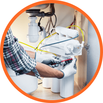 Plumber installing water filter under a sink, wearing gloves, with a red screwdriver.