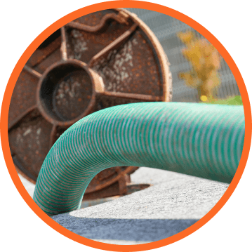 Green hose curves in front of a rusty metal spool, set on concrete.