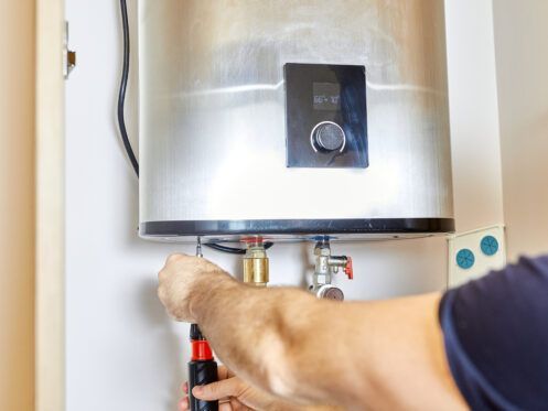 Person installing a water heater in a white cabinet, using a screwdriver.