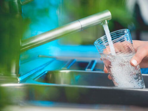 Person filling a glass with water from a faucet in a kitchen sink.