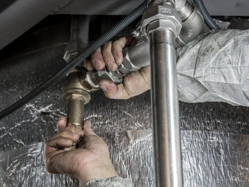Hands of a plumber tightening a metal pipe fitting in a mechanical room.