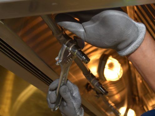Person wearing gray gloves uses a wrench to tighten a metal pipe inside a metallic setting.