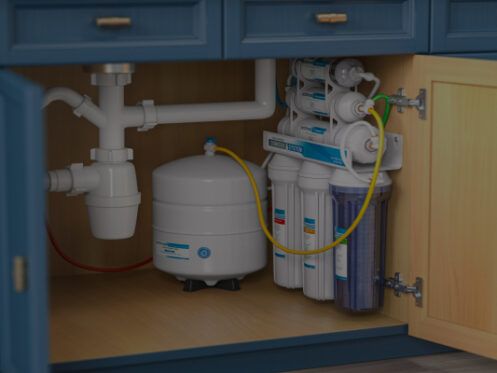 Reverse osmosis water filter system installed under a kitchen cabinet, with various filters and a storage tank.