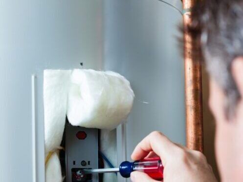 A person using a screwdriver to work on a water heater. The scene is indoors.
