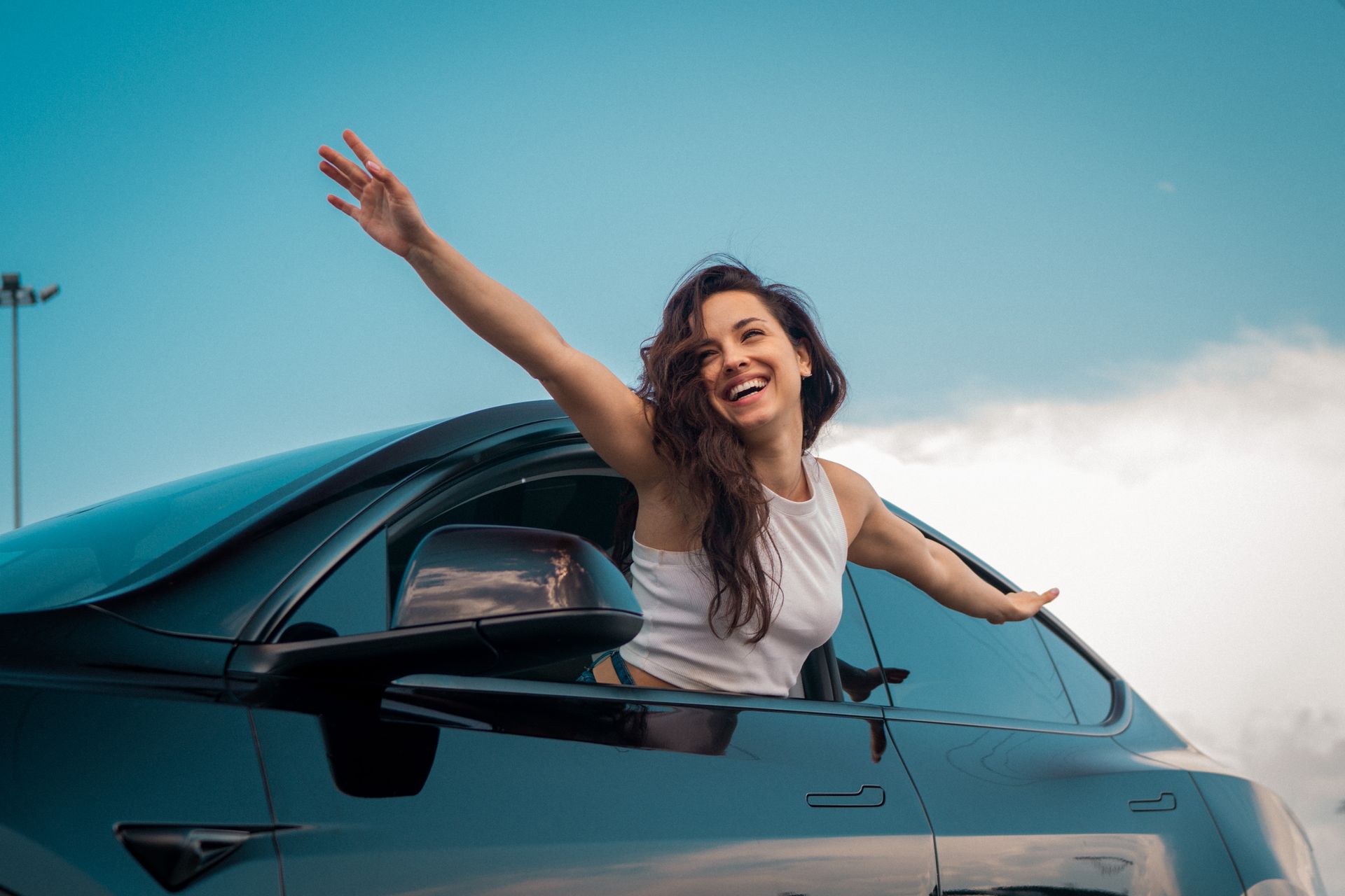 A woman is sitting in a car with her arms out the window.