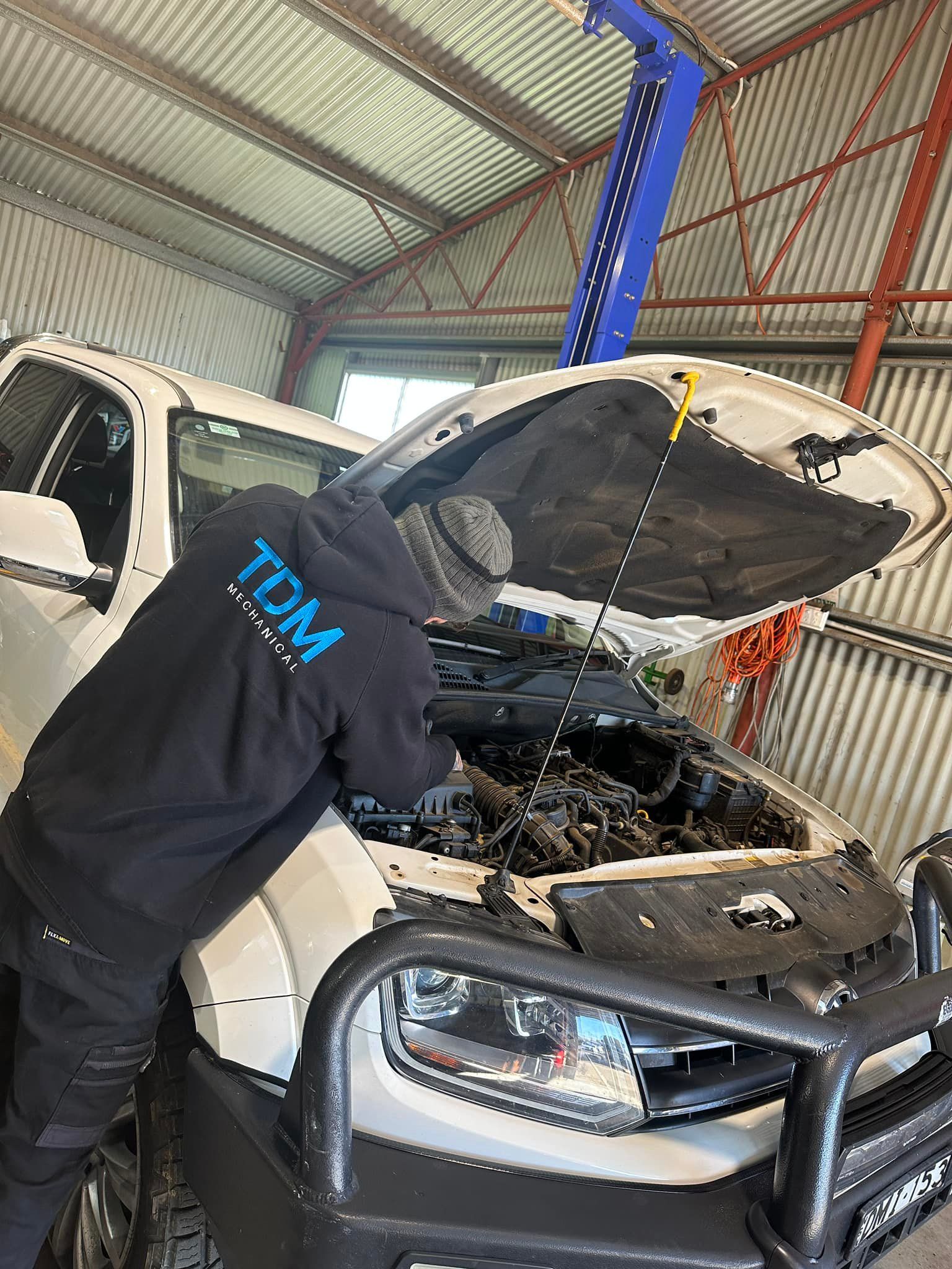 Mechanic in a Black  Working on a White Truck Engine in a Garage.