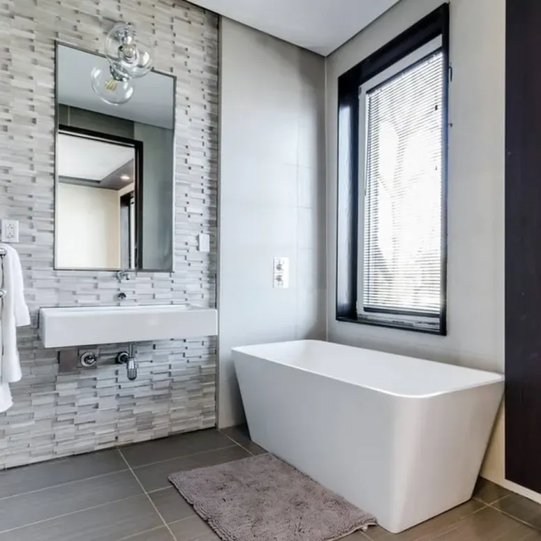 A bathroom with a tub , sink , mirror and window.