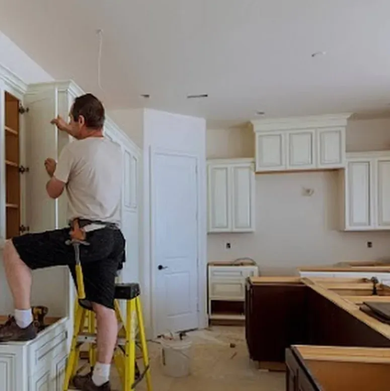 A man is standing on a ladder in a kitchen working on cabinets.