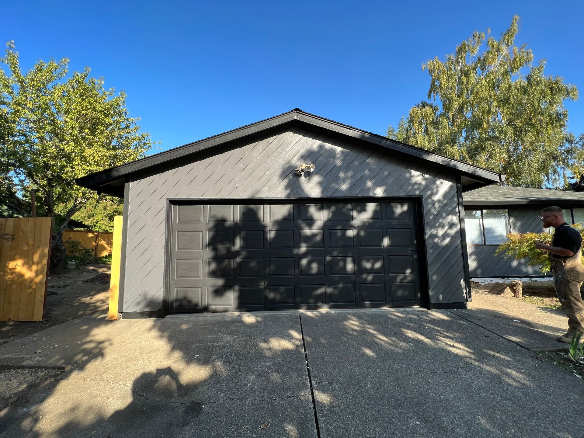 A man is standing in front of a gray garage with a black door.