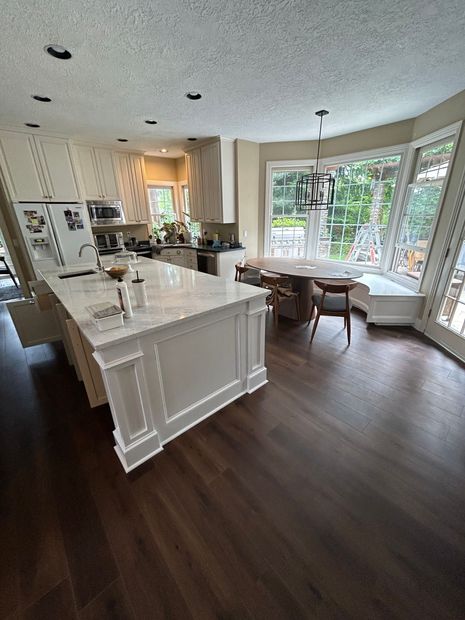 A kitchen with a large island , a table , chairs and a refrigerator.