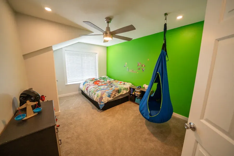 A bedroom with a green wall and a blue hammock hanging from the ceiling.
