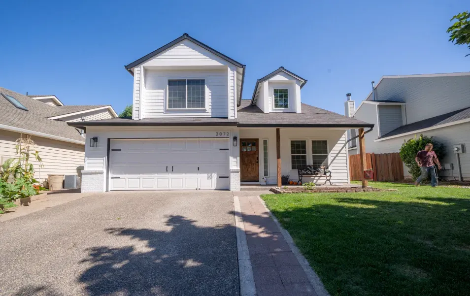 A white house with a large driveway and a man walking in front of it.