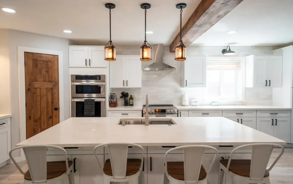 A kitchen with white cabinets , stainless steel appliances , a large island and chairs.