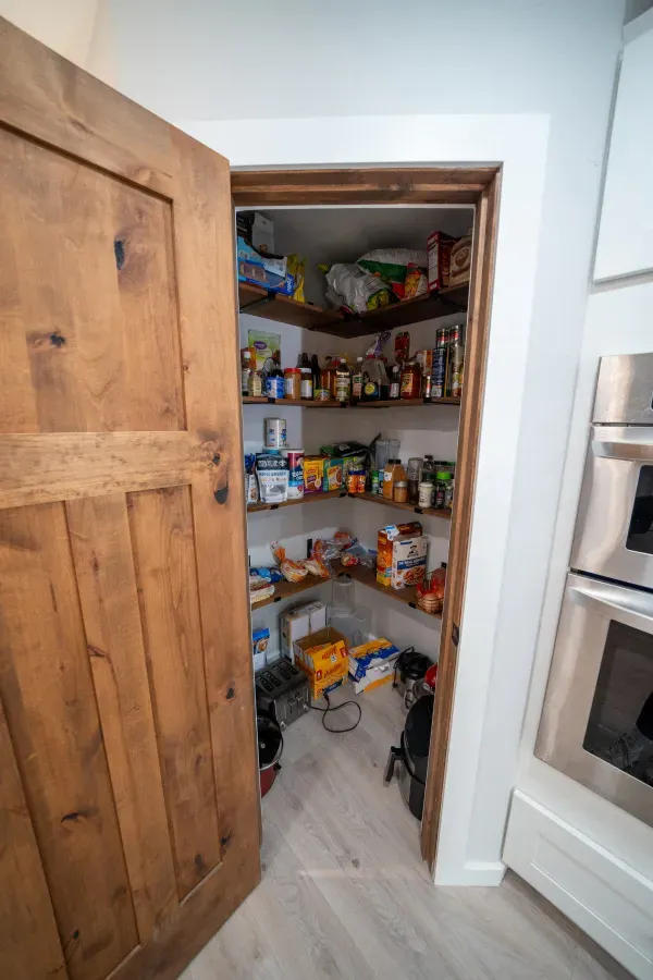 A pantry in a kitchen with a wooden door and shelves filled with food.