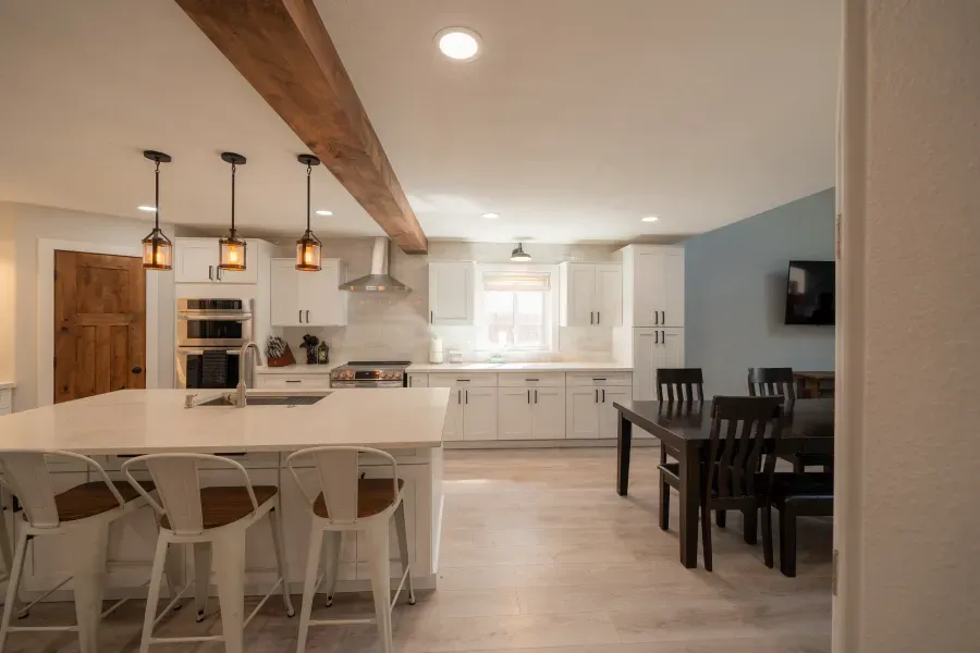 A kitchen with white cabinets , a large island , a table and chairs.