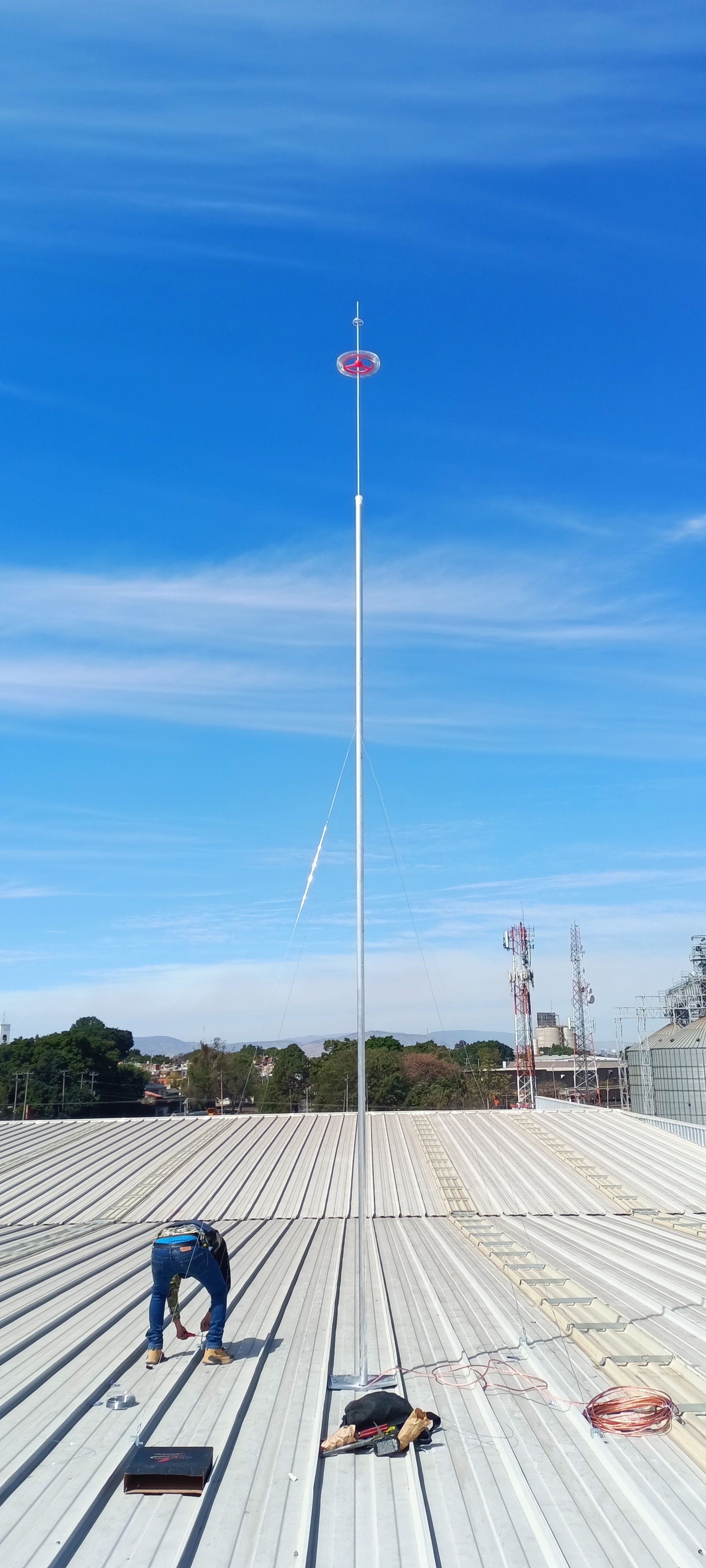 Un hombre está parado encima de un techo de metal trabajando en un pararrayos.
