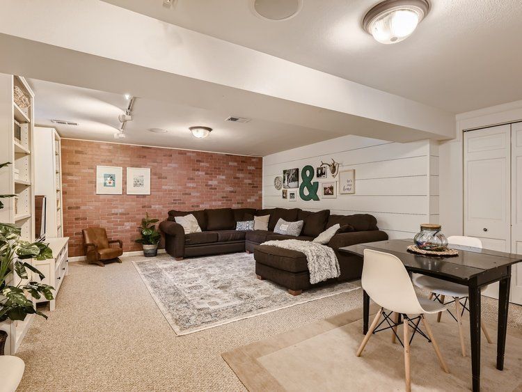 After Interior Design of Basement. Updated paint and shiplap wall. Modern furniture and decor. Large brown sectional and new faux brick accent wall.