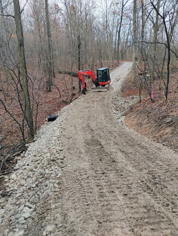 An orange excavator works on a gravel road in a wooded area.