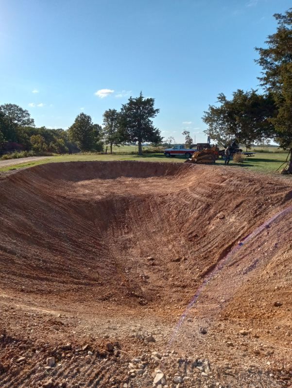 A large hole in the ground in a field with trees in the background.