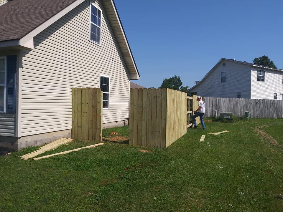 A man is standing next to a wooden fence in front of a house.