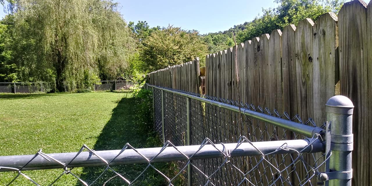 A chain link fence is surrounded by a wooden fence and a lush green field.