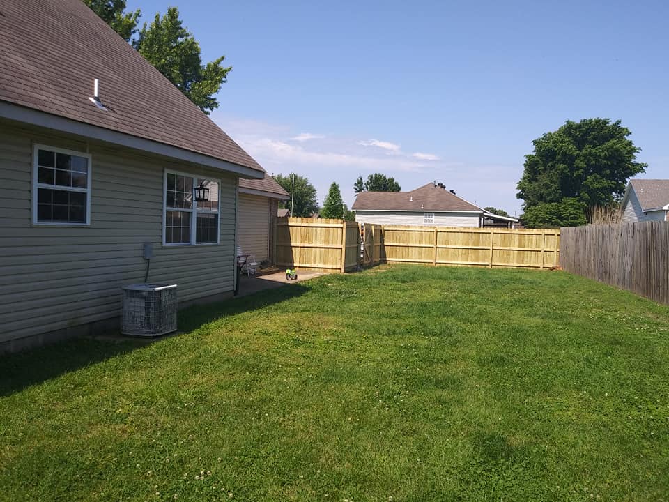 A backyard with a wooden fence and a house in the background