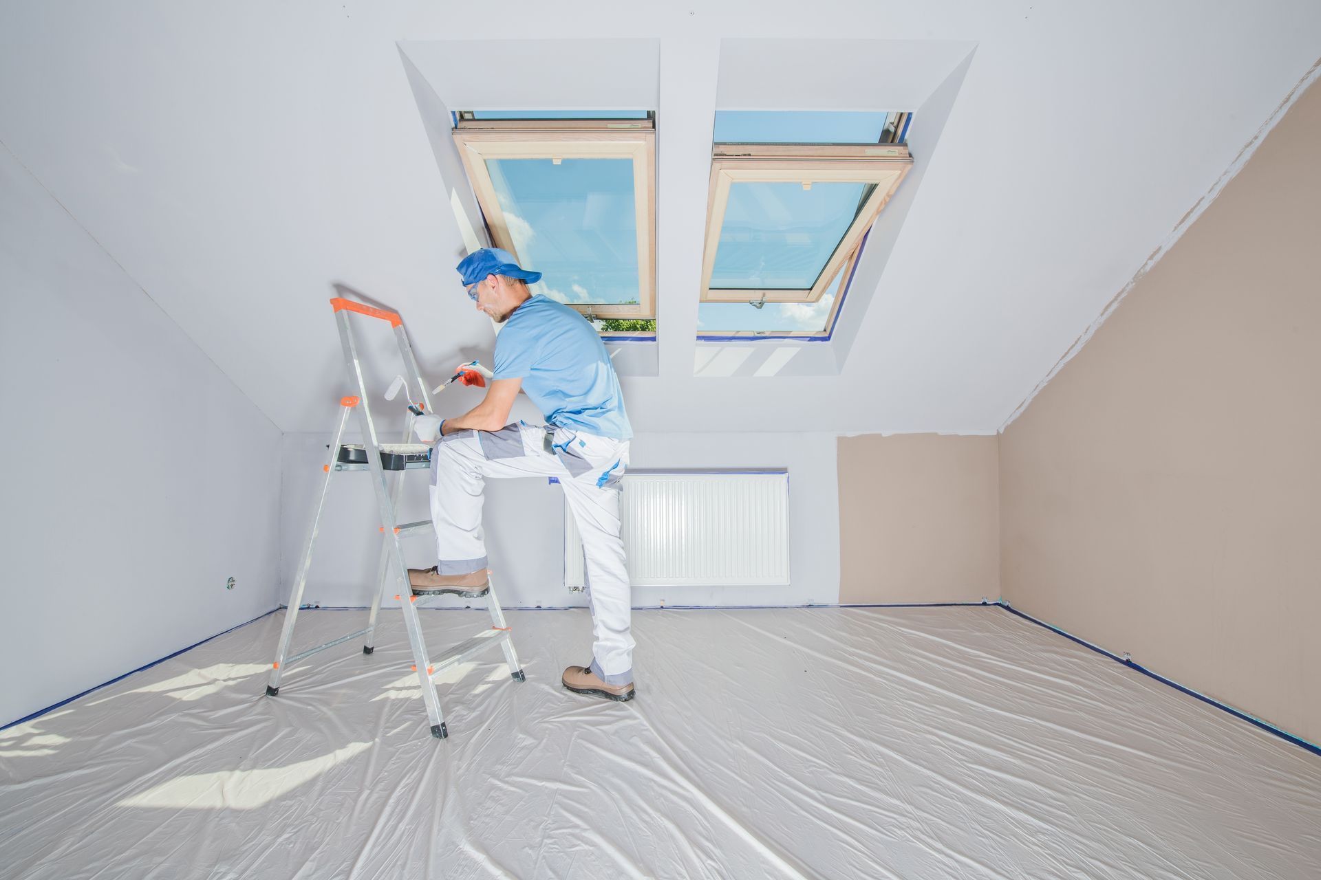 A man is sitting on a ladder in an empty room painting the ceiling.