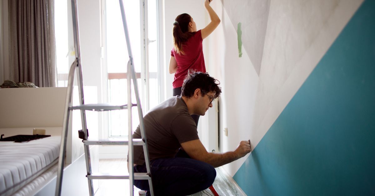 A man and a woman are painting a wall in a bedroom.