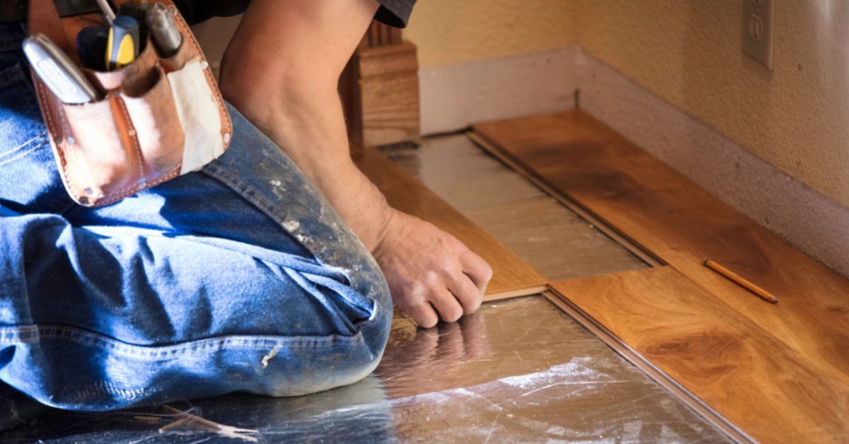A man is kneeling on the floor while installing a wooden floor.