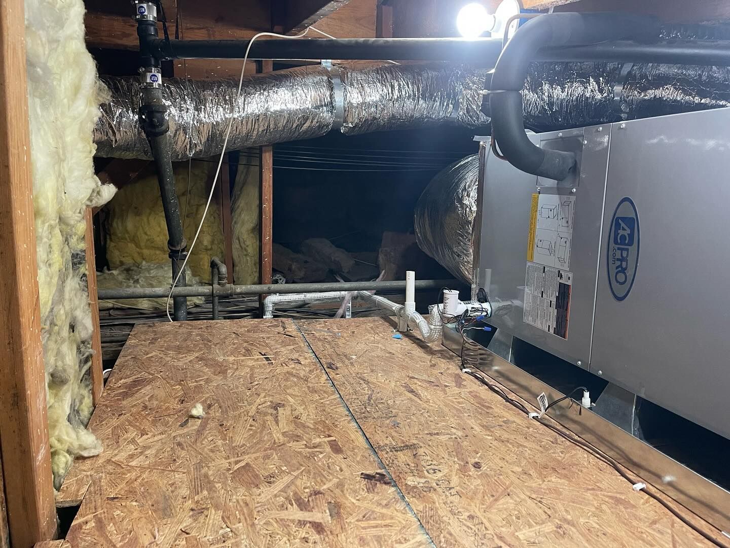 Attic with ductwork, insulation, and HVAC unit on a wooden platform.