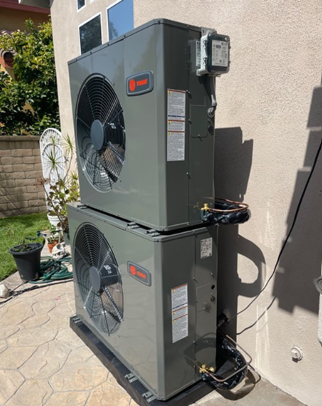 Two stacked gray Trane air conditioning units on a patio next to a wall.