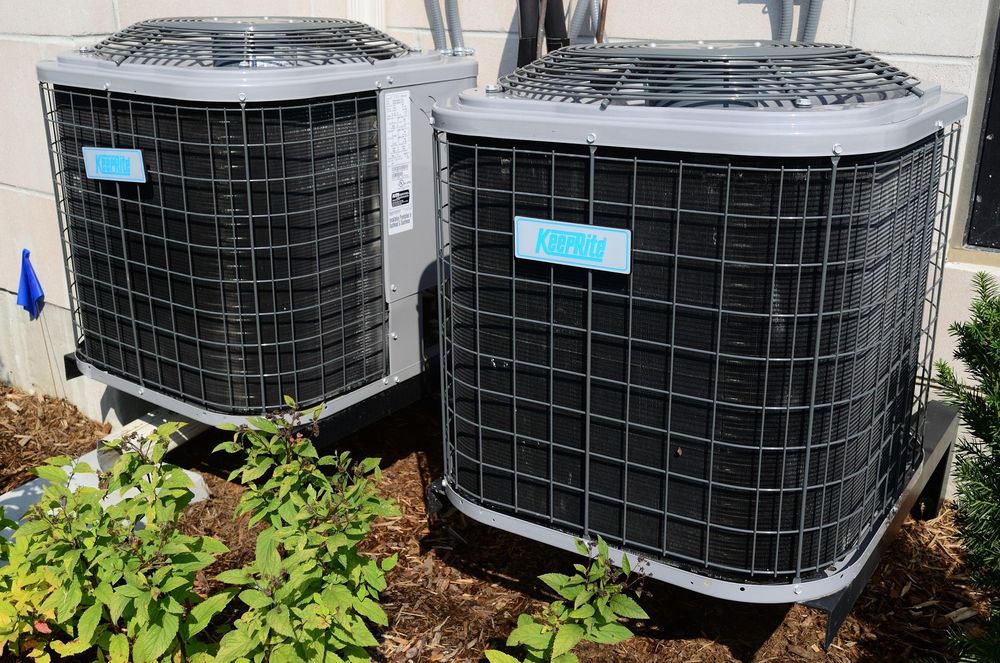 Two outdoor air conditioning units near bushes.