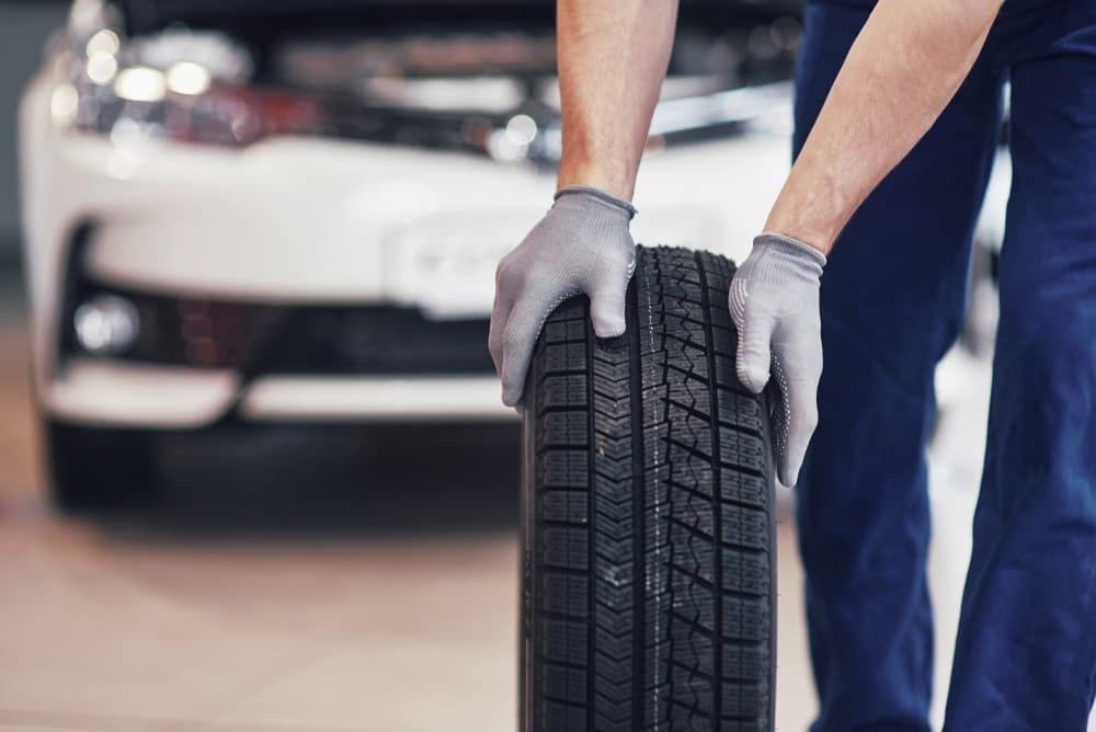 A Man Is Holding A Tire In Front Of A Car — Banora Automotive In Tweed Heads South, NSW
