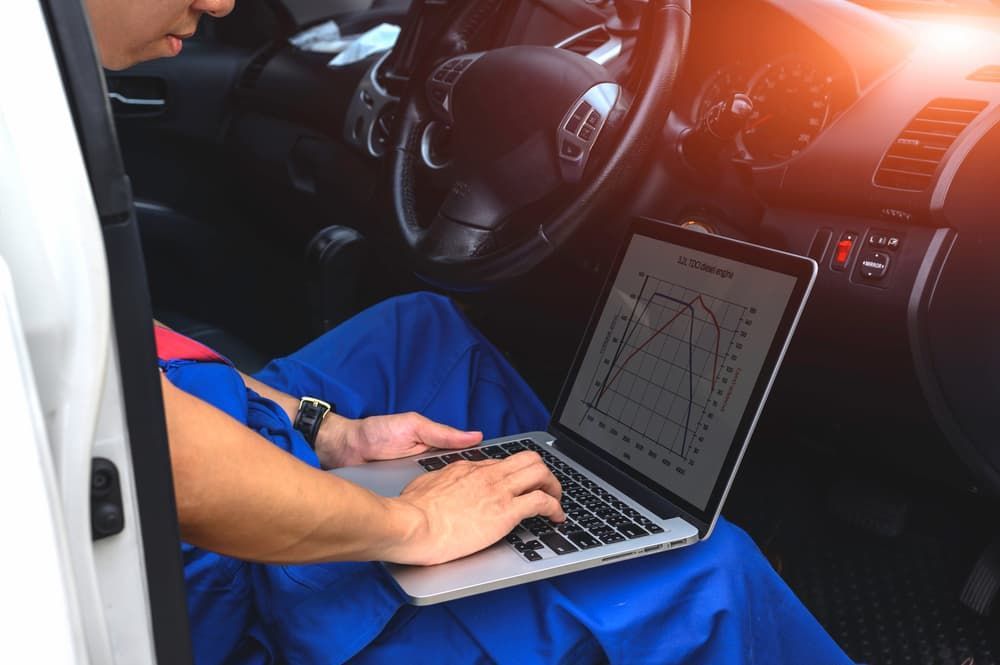 A Man Is Sitting In A Car Using A Laptop Computer To Check The Car Program — Banora Automotive In Tweed Heads South, NSW