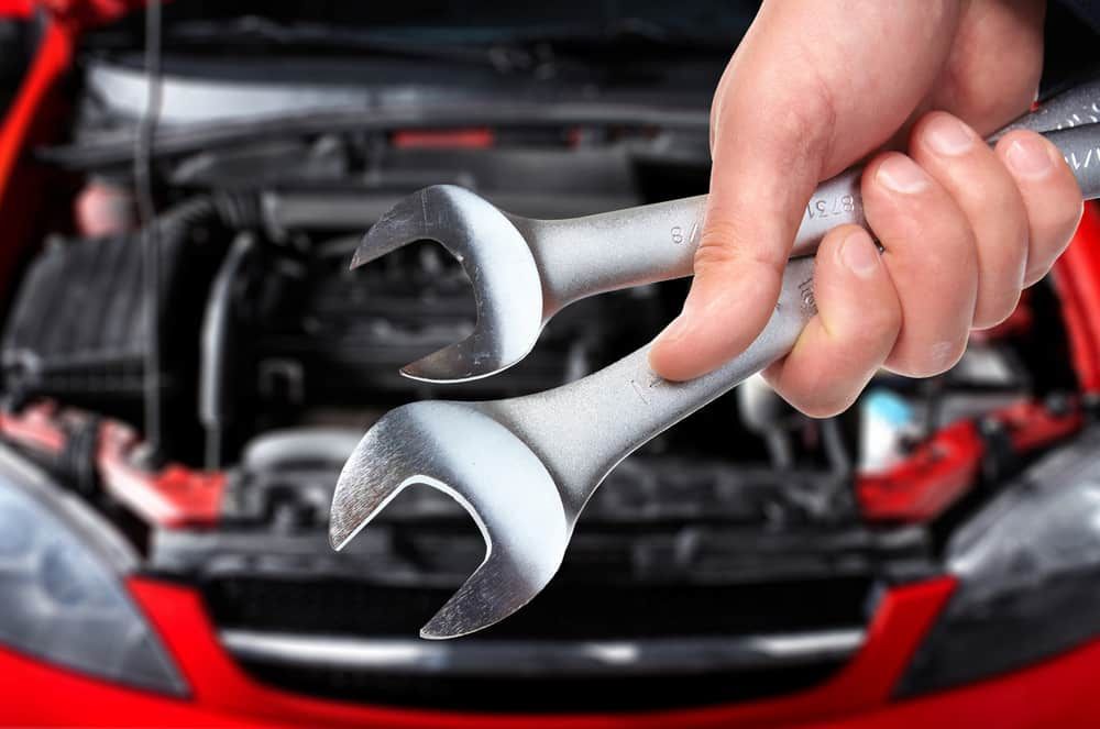 A Person Is Holding Two Wrenches In Front Of A Red Car — Banora Automotive In Tweed Heads South, NSW