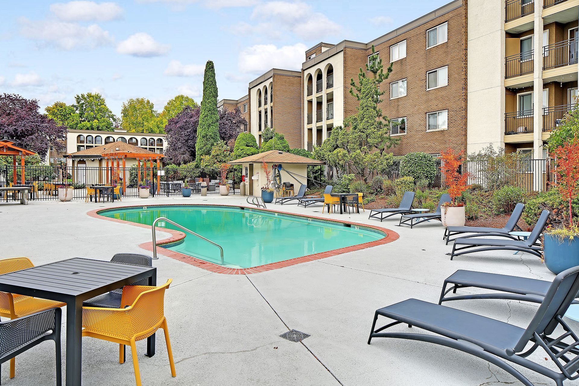 A large swimming pool surrounded by chairs and tables in front of a building.