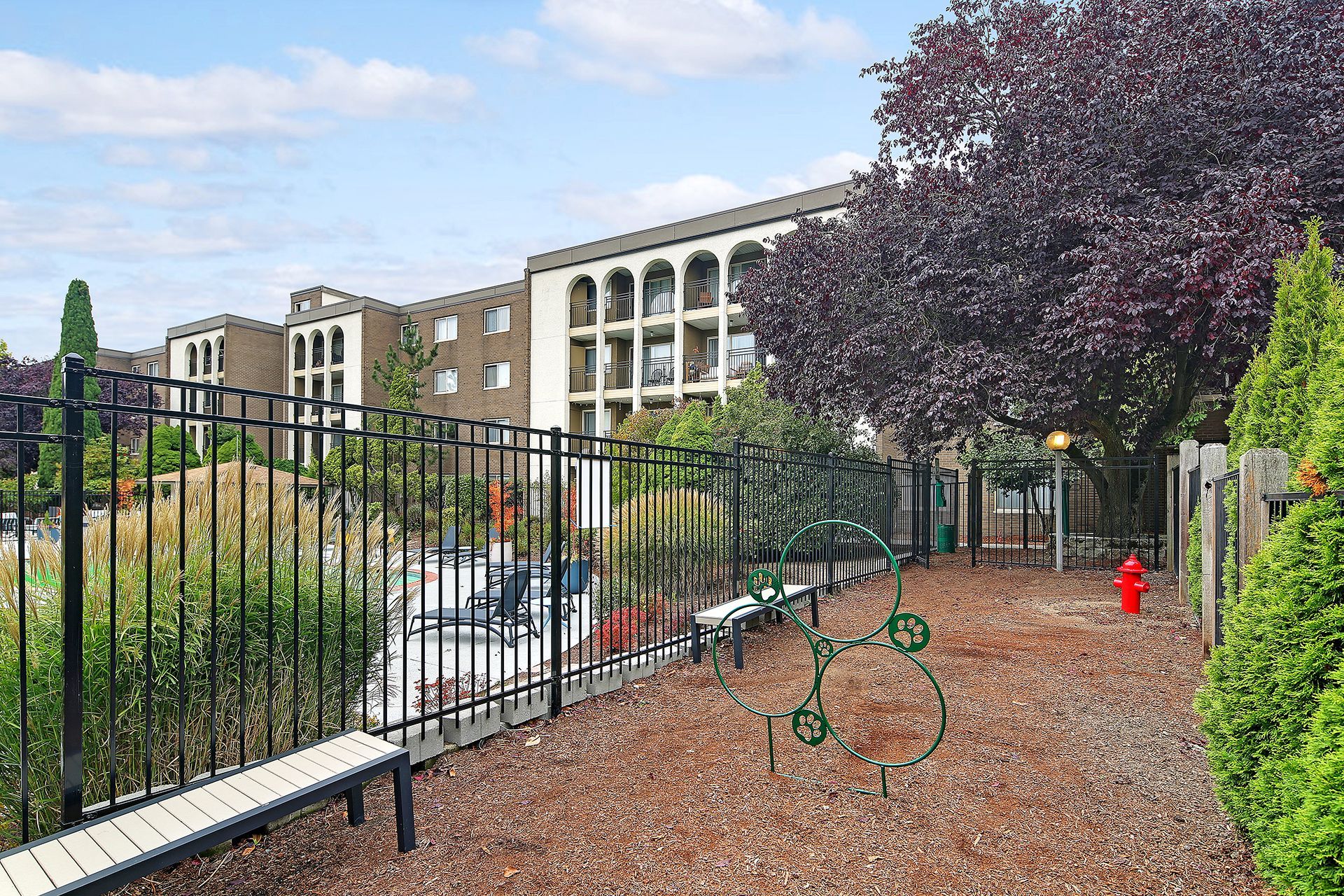 A park with a bench and a fire hydrant in front of a building.