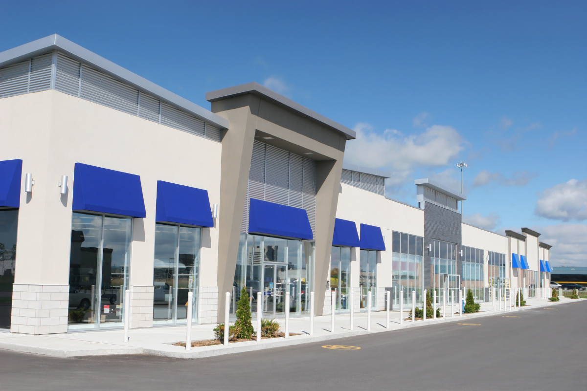 Strip mall with blue awnings over large windows, on a sunny day.