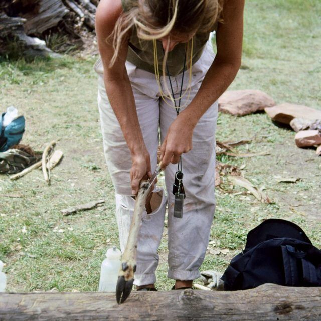 A woman in white pants is standing on a log holding a hammer
