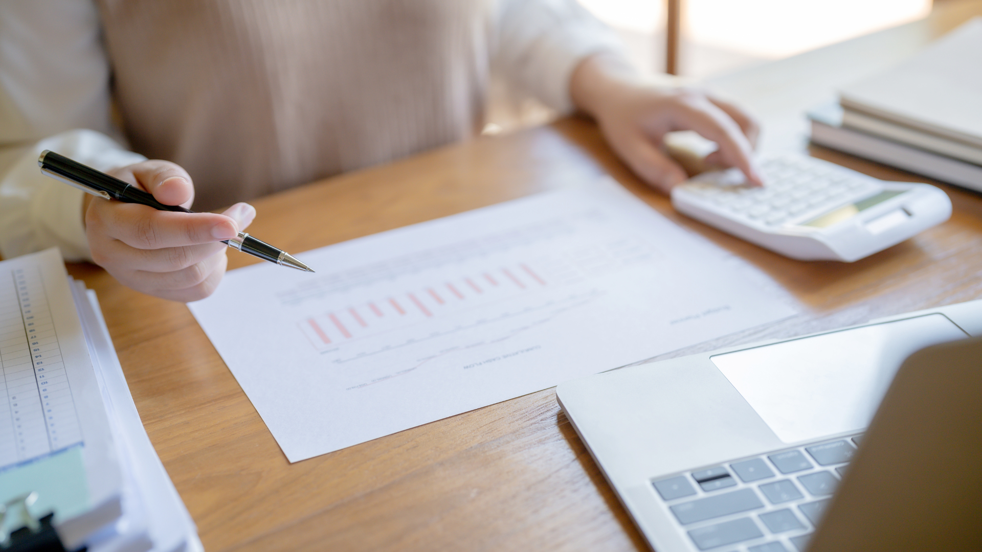 A woman is sitting at a desk using a calculator and a pen.